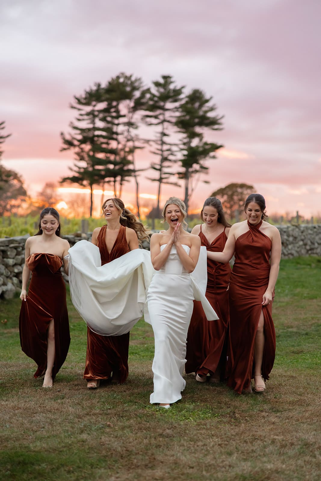 Bride walking with bridesmaids at golden hour in the vineyard at one of the most romantic wedding venues in Rhode Island.