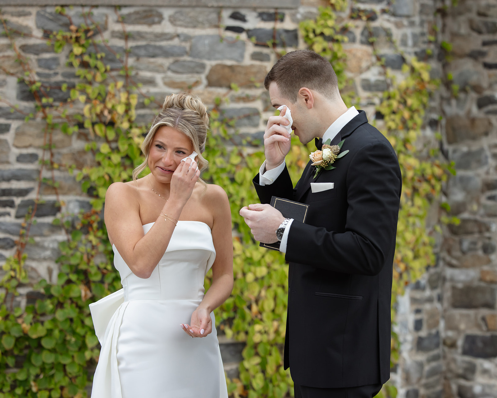 Bride and groom wiping tears while reading vows against ivy-covered stone wall at one of the most intimate wedding venues in Rhode Island.