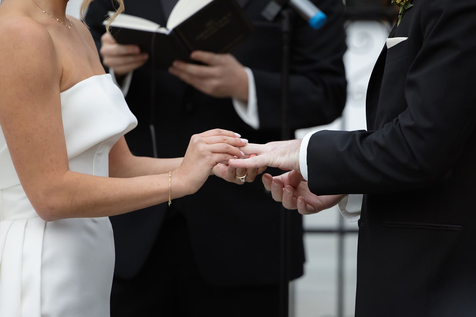 Close-up of bride placing wedding band on groom’s hand during outdoor ceremony at one of the most timeless wedding venues in Rhode Island.