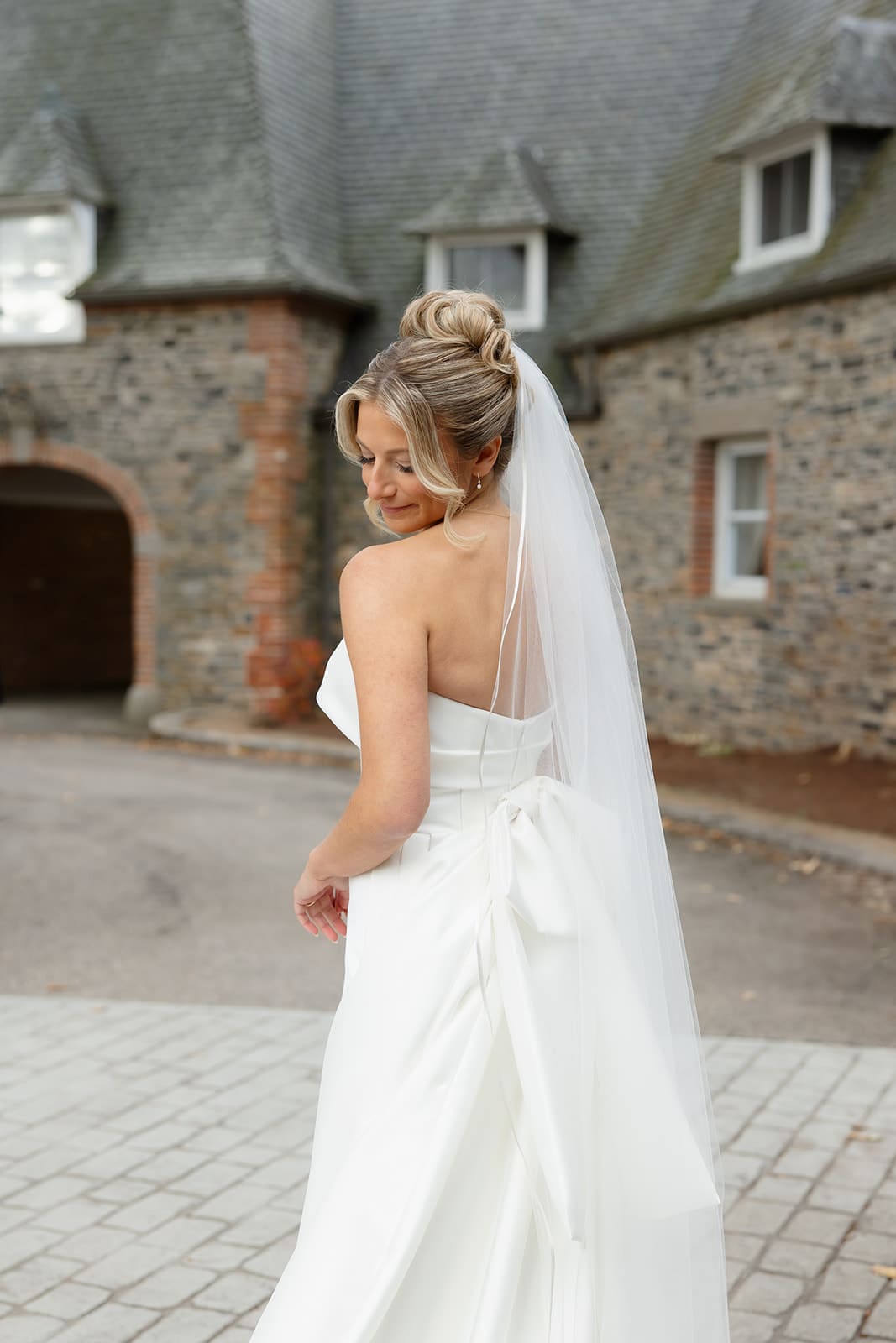 Bride looking back over her shoulder with a long veil outside a historic estate, one of the timeless Wedding Venues in Rhode Island.
