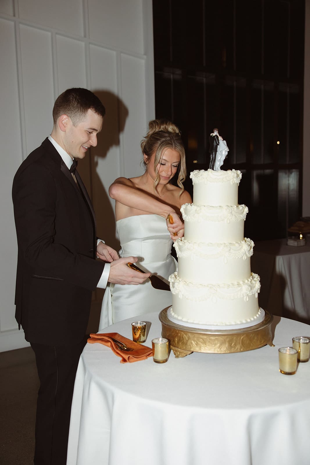 Bride and groom cutting four-tier wedding cake during candlelit reception at a Rhode Island wedding venue.