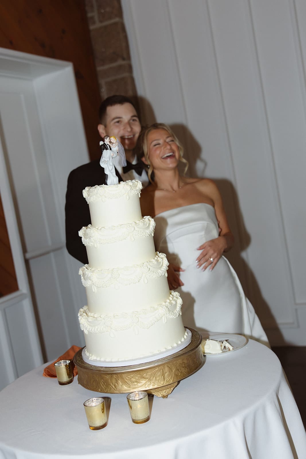 Bride and groom laughing behind four-tier white wedding cake at one of the most elegant wedding venues in Rhode Island.