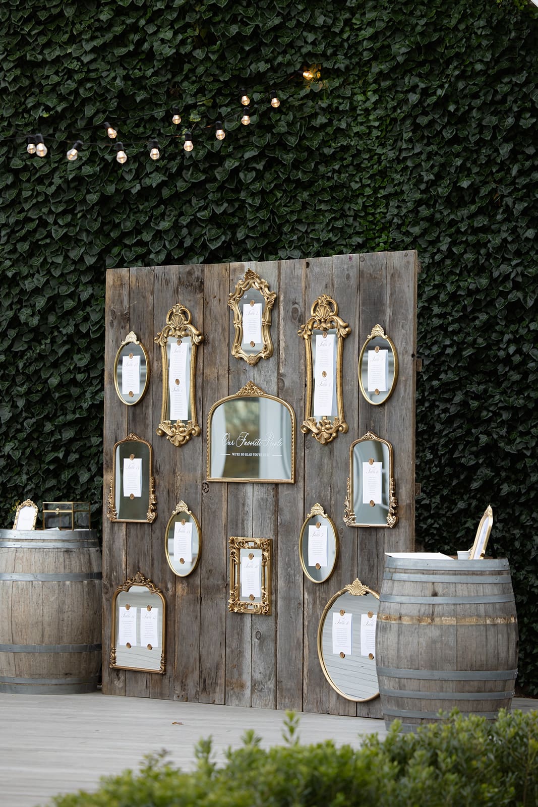 Elegant seating chart display with gold frames and mirrors set against ivy wall at a Rhode Island wedding venue.