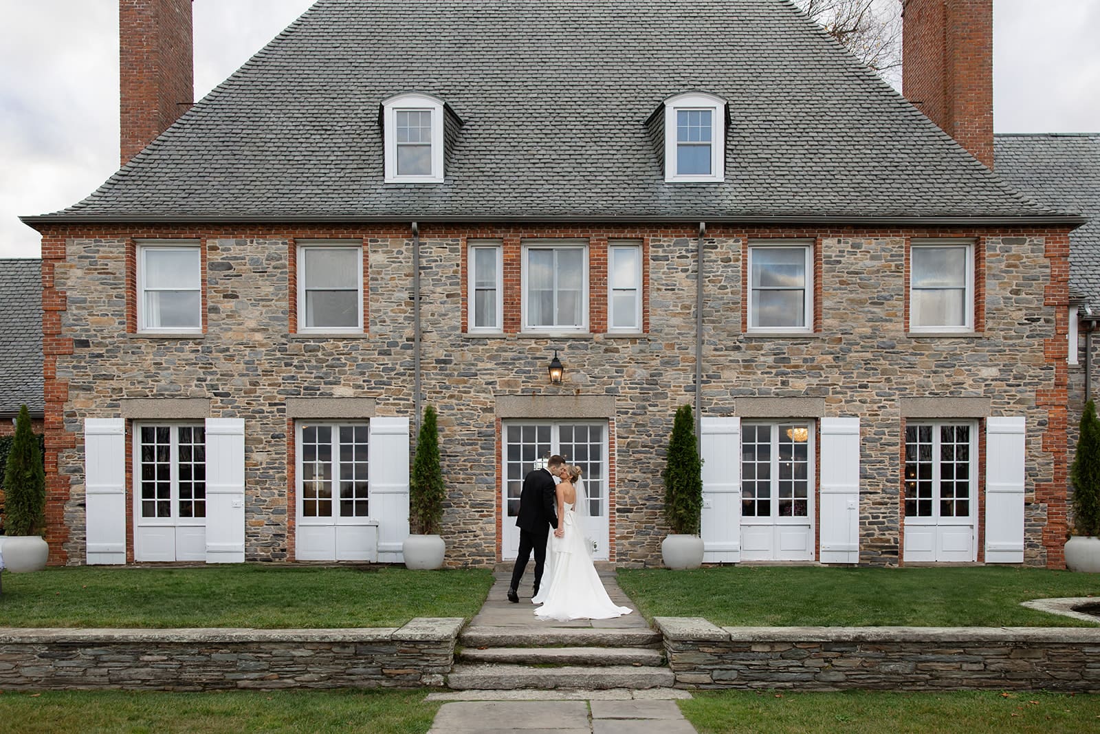 Bride and groom standing together in front of a grand stone estate, showcasing one of the most timeless Wedding Venues in Rhode Island.
