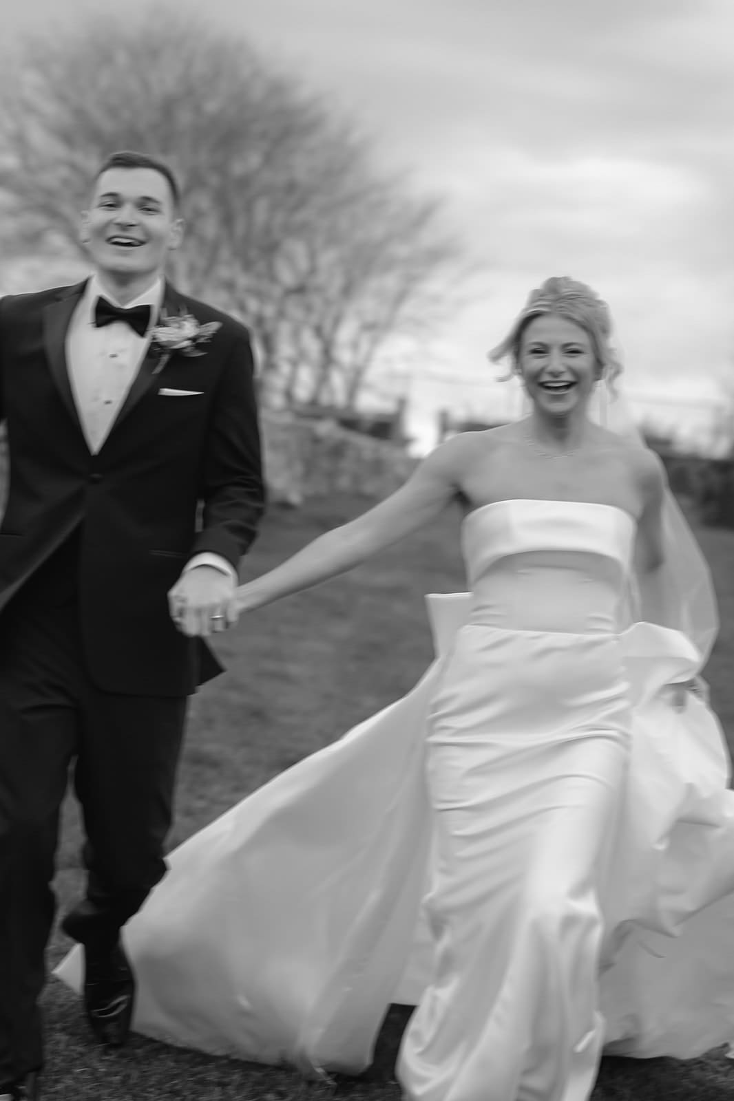 Bride and groom running hand in hand across estate lawn in joyful black and white portrait.