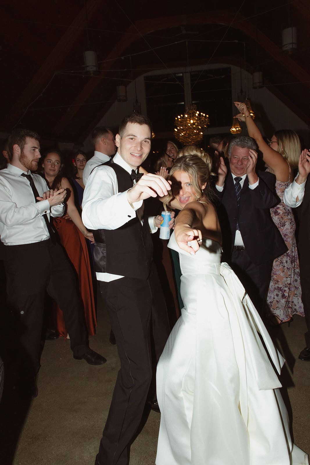 Bride and groom leading packed dance floor celebration under chandeliers at a Rhode Island estate reception.