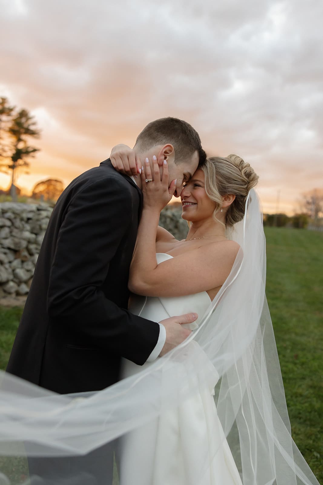 Bride holding groom’s face as her veil moves in the sunset light at one of the most timeless wedding venues in Rhode Island.