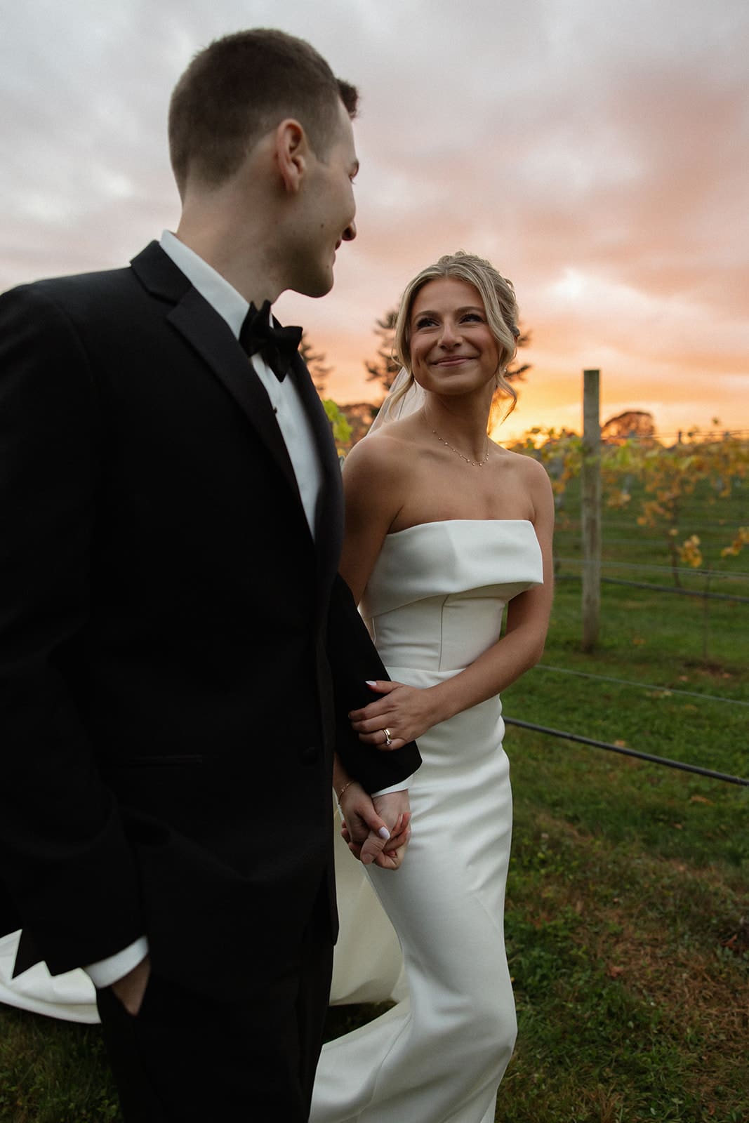 Bride smiling at groom as they walk through vineyard at sunset at one of the most romantic wedding venues in Rhode Island.