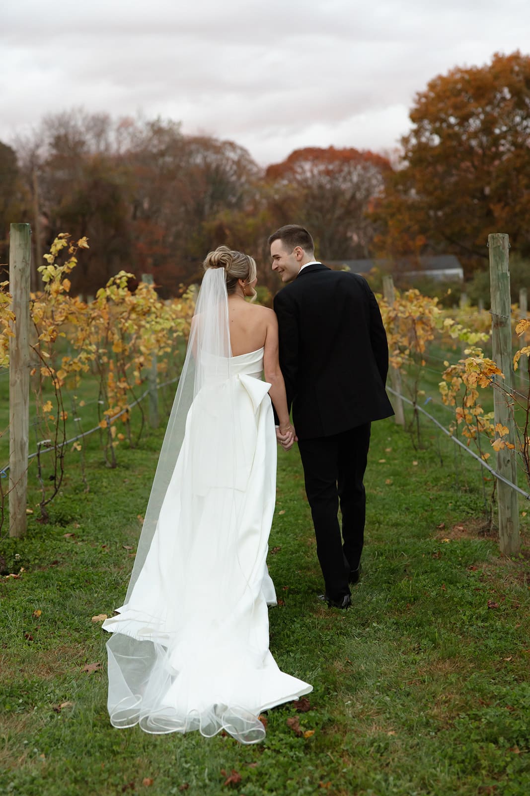 Bride and groom walking hand in hand through autumn vineyard rows at one of the most scenic wedding venues in Rhode Island.