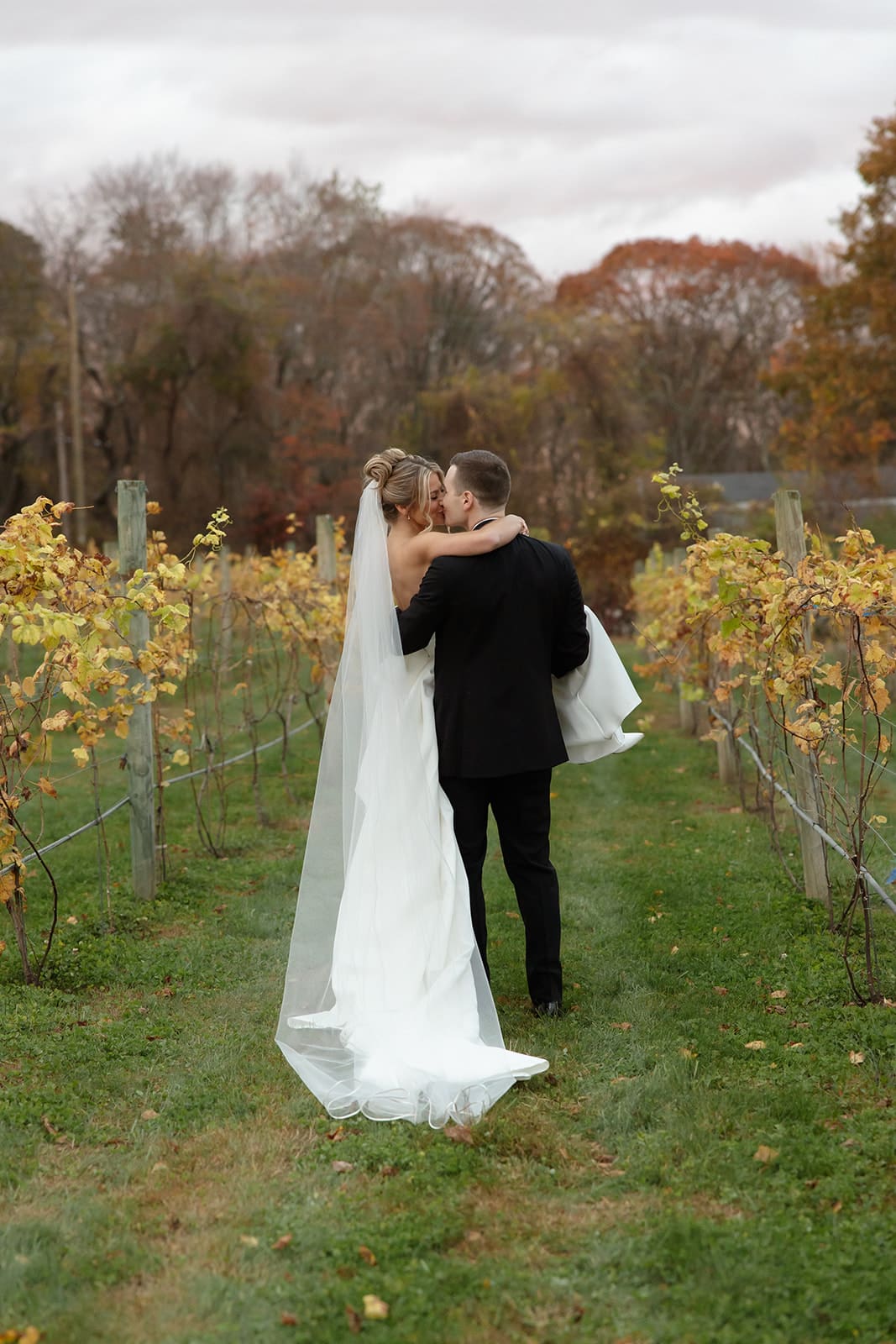 Bride wrapping her arms around groom as they walk through vineyard at one of the most elegant wedding venues in Rhode Island.