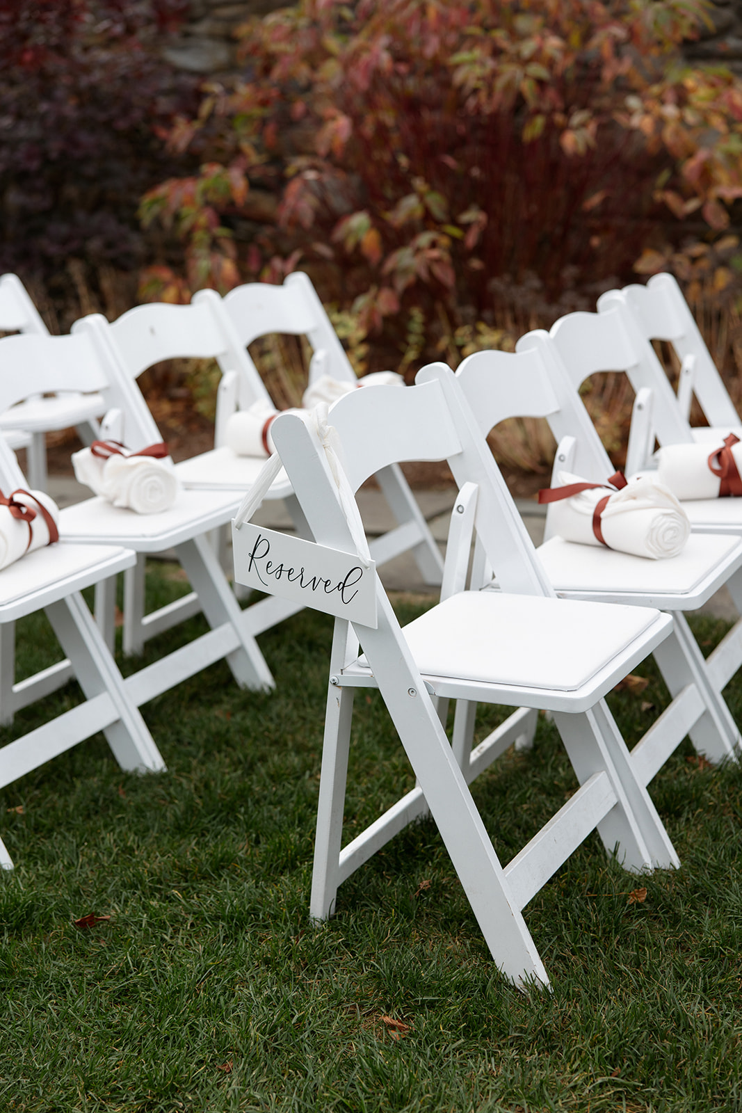 White ceremony chairs with reserved signs arranged on lawn for outdoor estate wedding.
