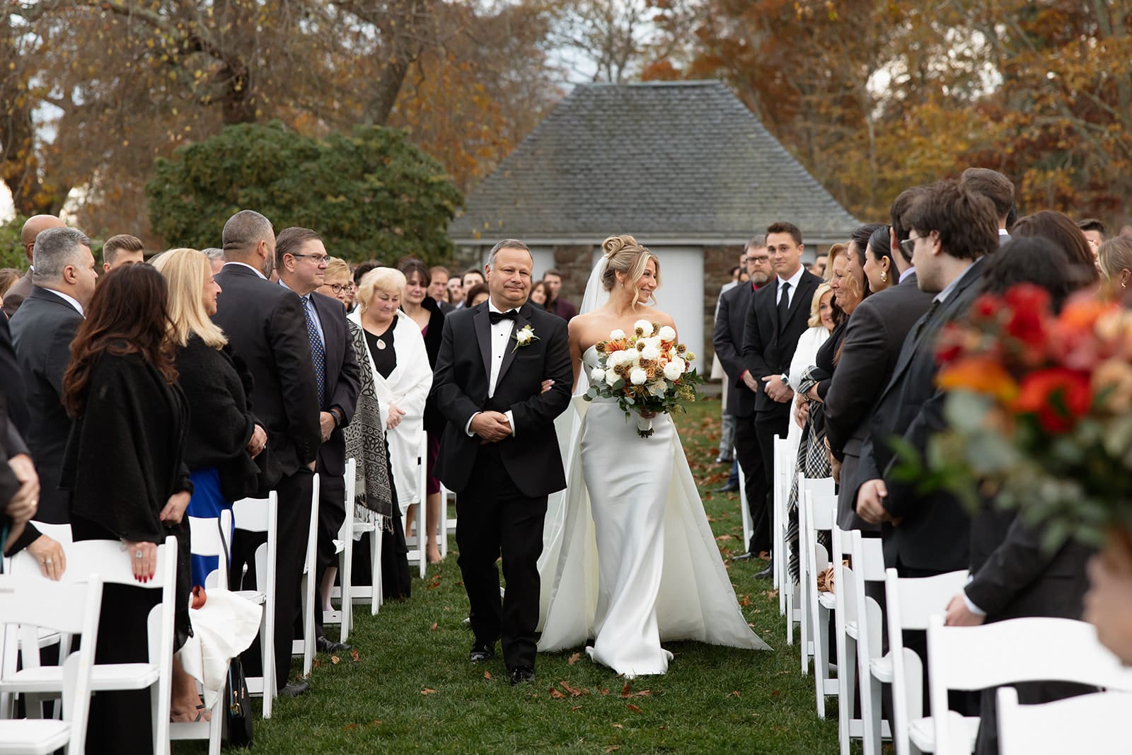 Bride walking down grassy aisle with her father surrounded by guests at a romantic Rhode Island estate wedding.