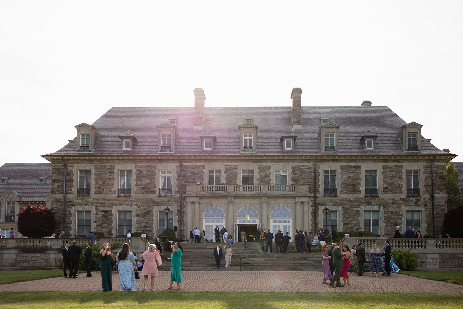 Guests mingle on the lawn in front of the estate as the sun sets, marking the start of a colorful wedding evening.
