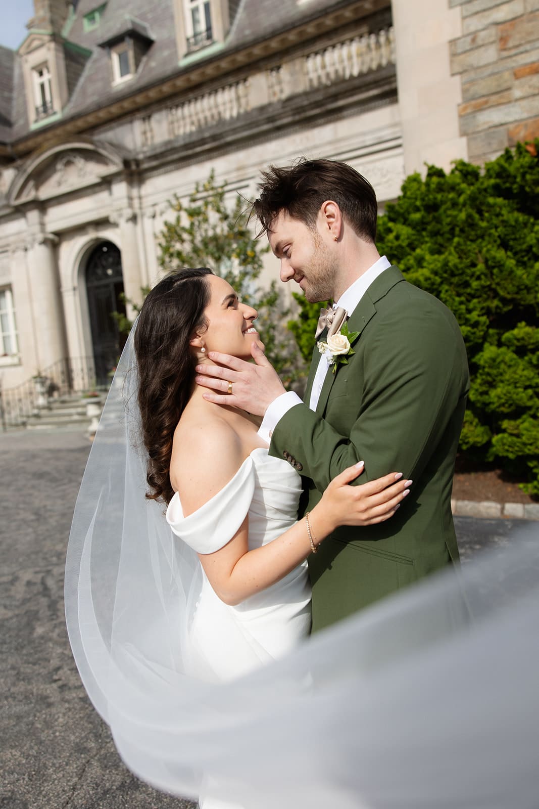 The couple stands close together outside the estate, the bride’s veil moving gently in the light during a colorful wedding.
