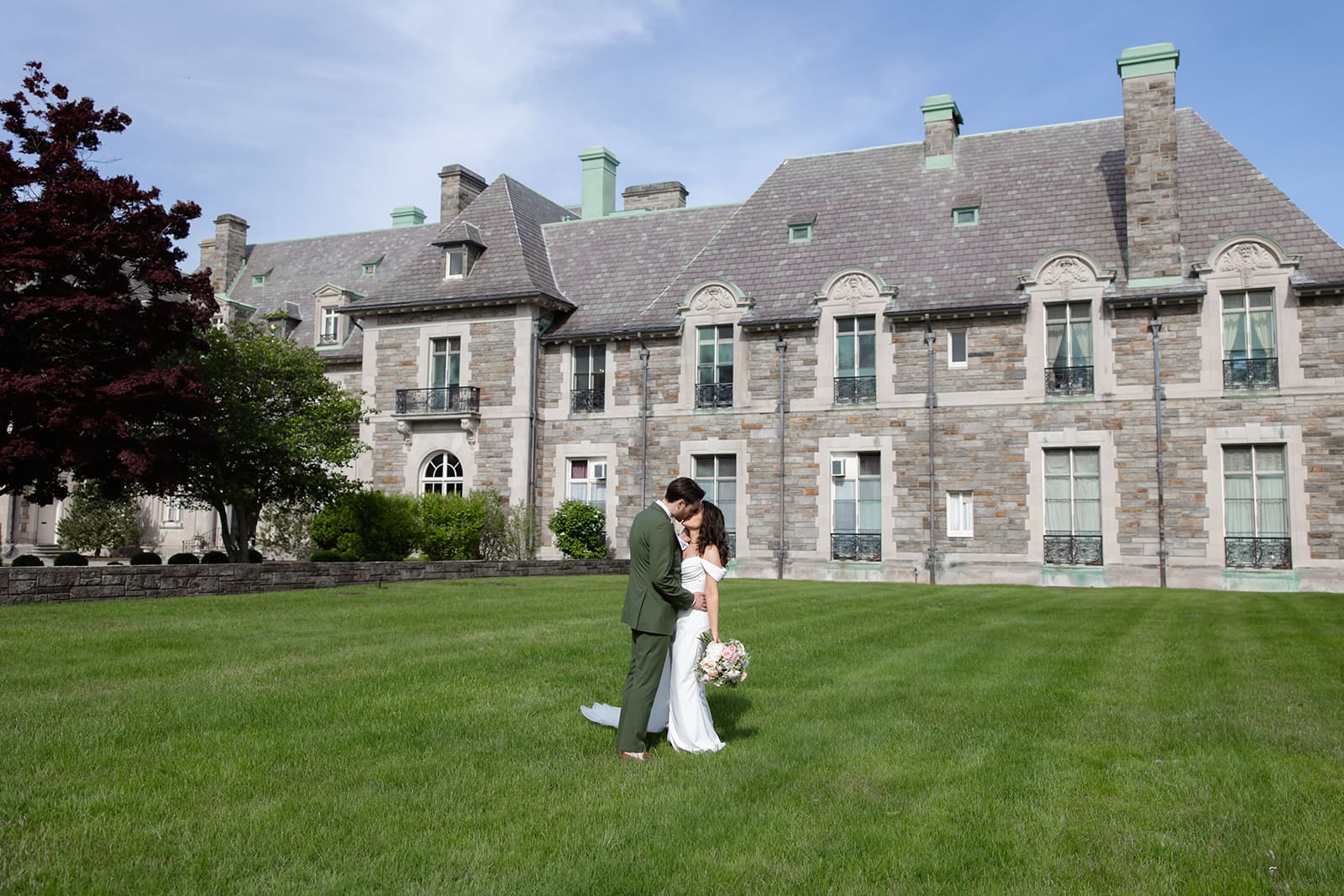 The couple stands together on the lawn in front of the estate, sharing a quiet moment during a colorful wedding day.
