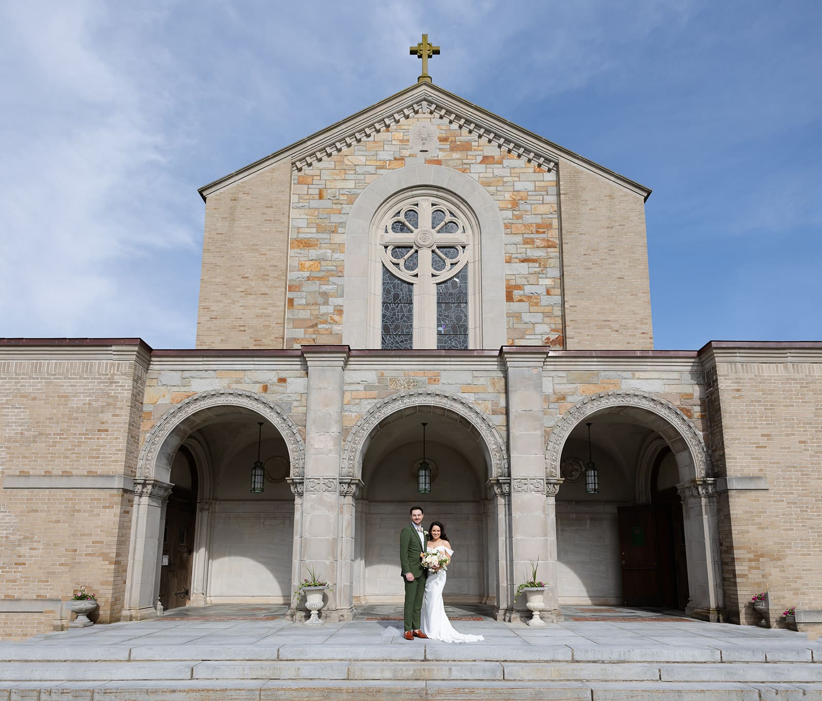 The bride and groom stand beneath the church arches, framed by the architecture during a colorful wedding day.
