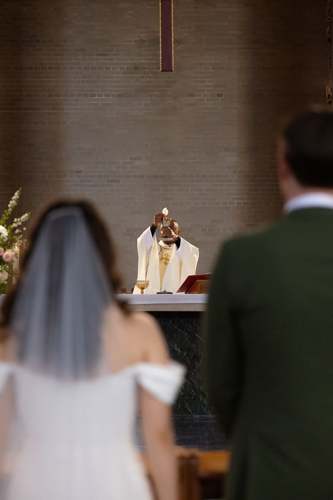 The priest lifts the Eucharist at the altar as the couple stands together during a colorful wedding ceremony.
