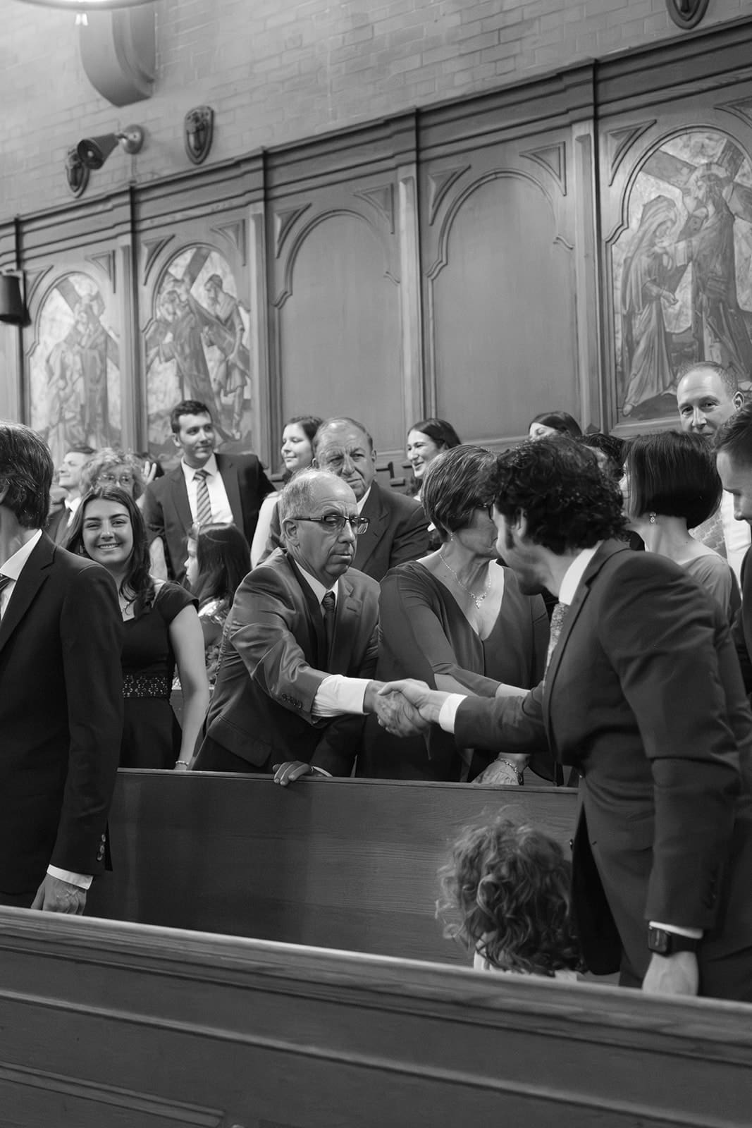 Guests greet one another inside the church, exchanging handshakes and quiet conversation before the ceremony.
