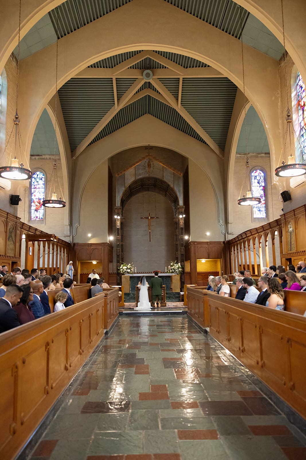 A wide view of the church interior as the ceremony unfolds, guests seated along the aisle during a colorful wedding.
