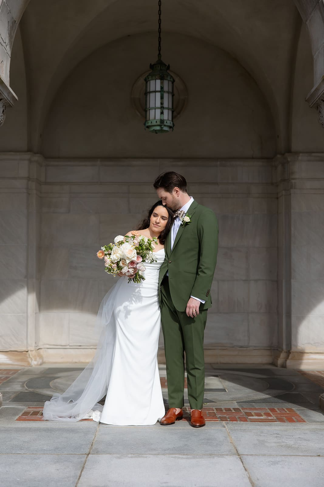 A quiet portrait of the couple beneath an arched stone entryway, the bride leaning gently into the groom.
