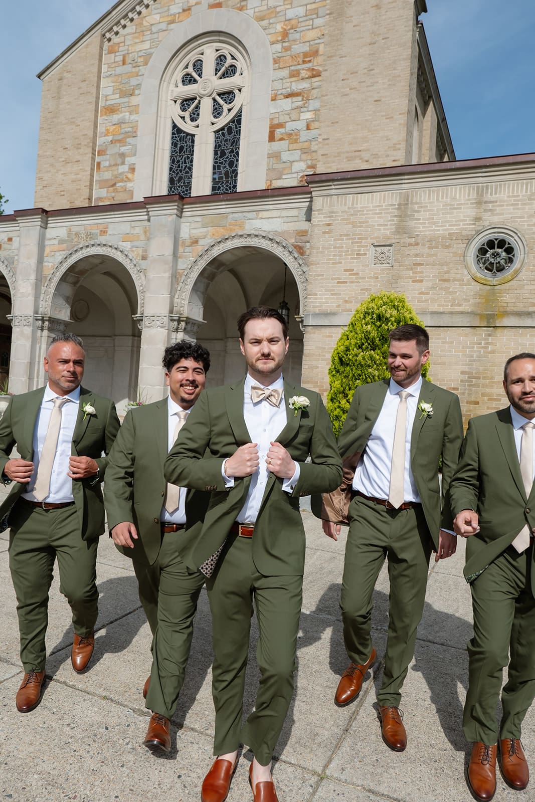 The groom and groomsmen walk together outside the church, their green suits adding a distinct look to a colorful wedding.
