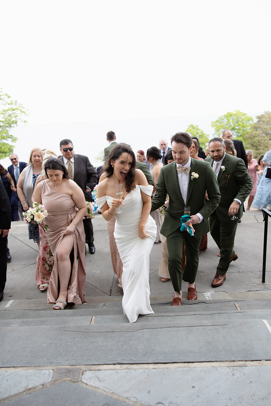 The bride and groom lead guests up the steps, laughing and holding drinks as the celebration continues.

