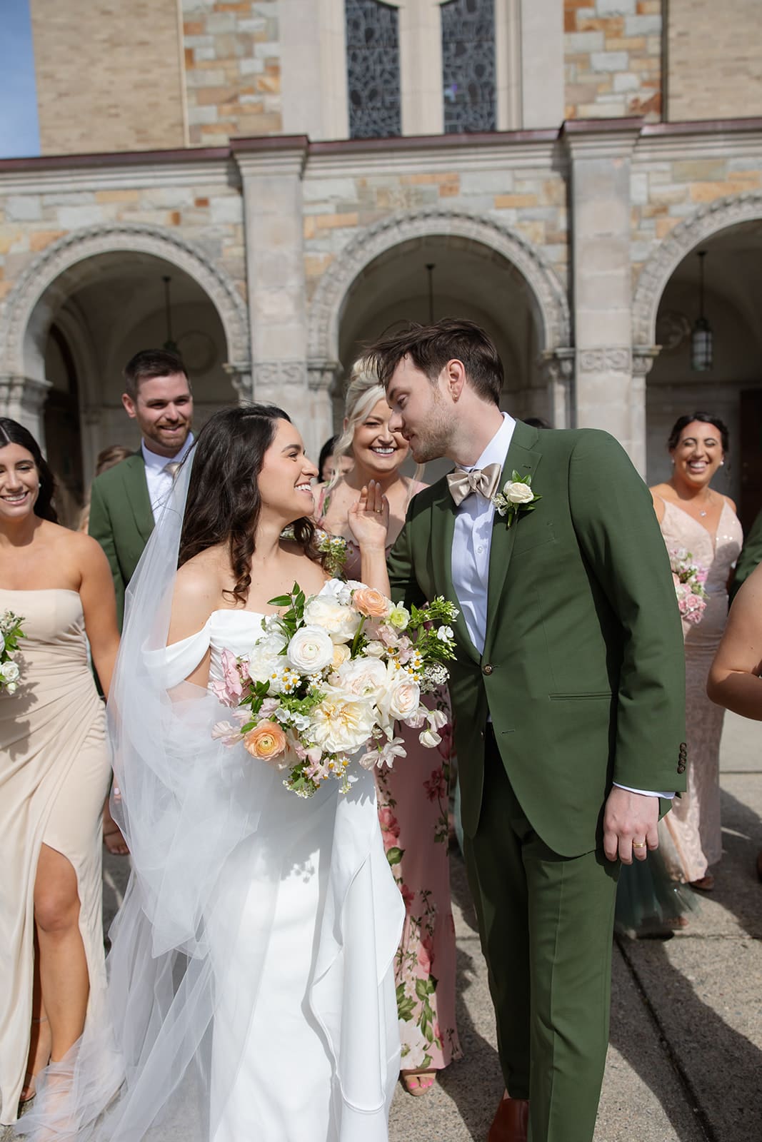 The couple walks out of the ceremony surrounded by their wedding party, smiling and relaxed in a colorful wedding celebration.
