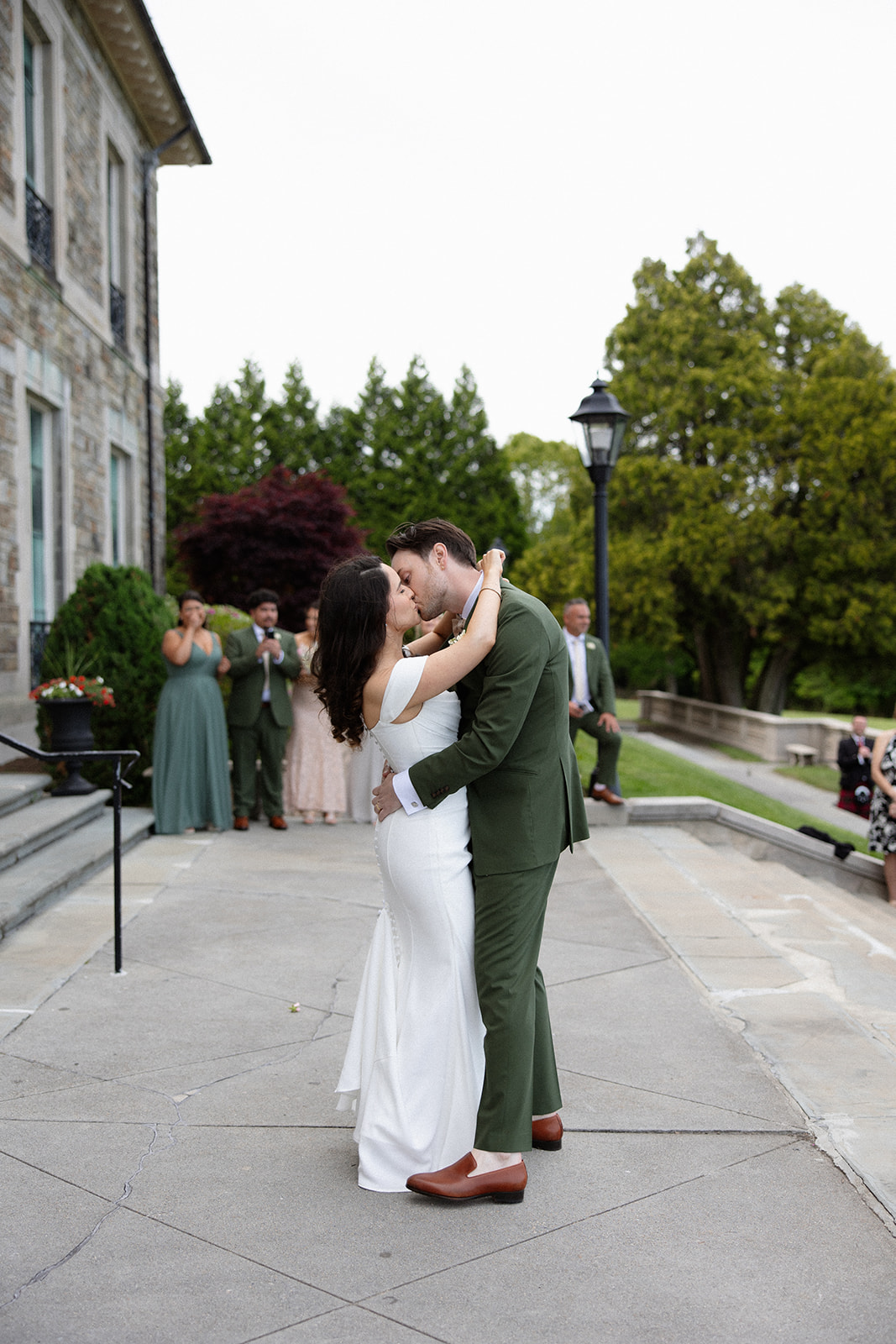 The couple shares a quiet embrace just outside the venue while guests watch from a distance during a colorful wedding.
