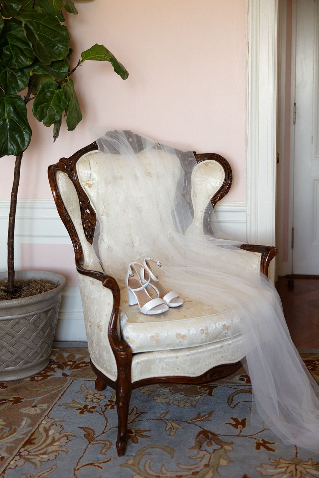 The bride’s veil and shoes rest on a vintage chair, a quiet detail from a colorful wedding morning.

