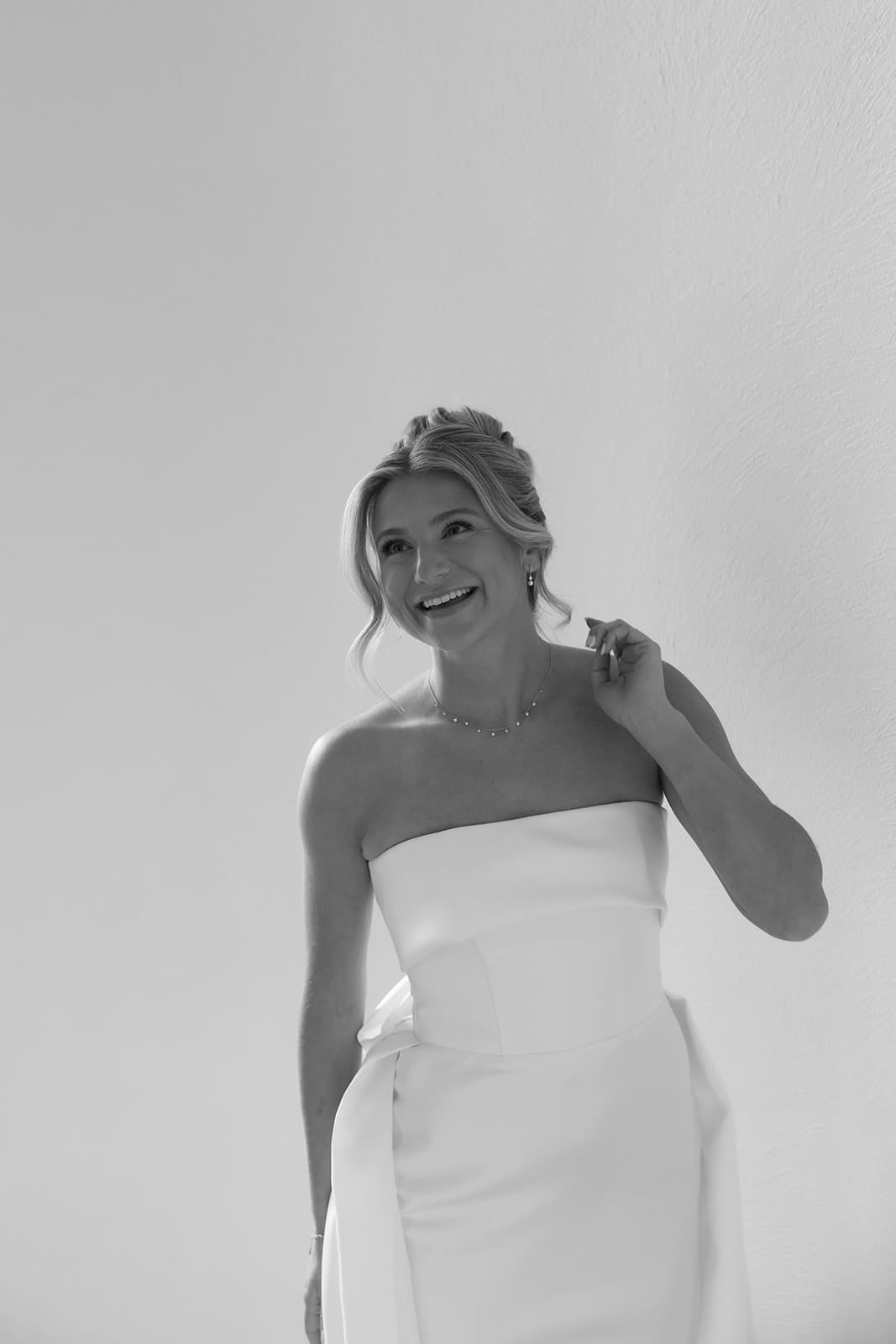 Black and white bridal portrait of a smiling bride in a minimalist strapless wedding gown.
