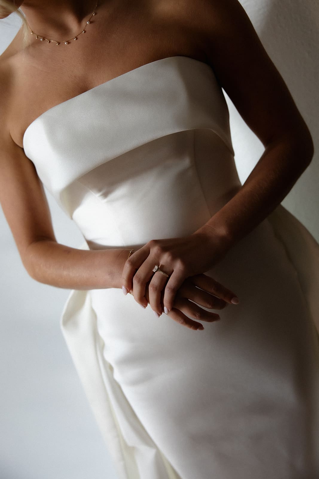 Close-up of a modern strapless wedding gown and engagement ring with soft natural light and elegant bridal styling.
