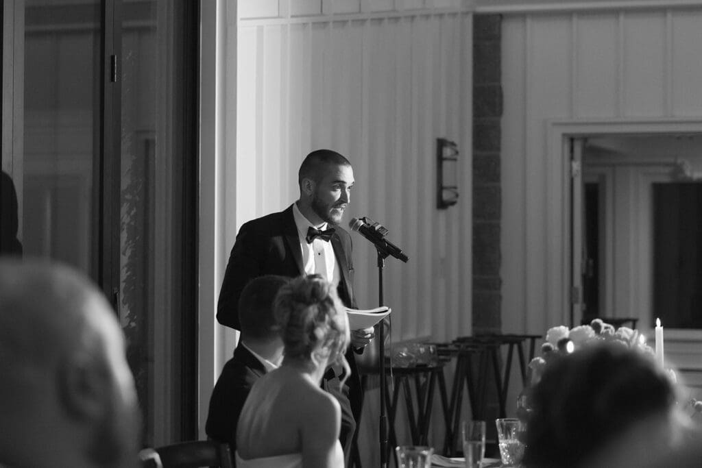 Black and white photo of the best man giving a heartfelt speech during the wedding reception.
