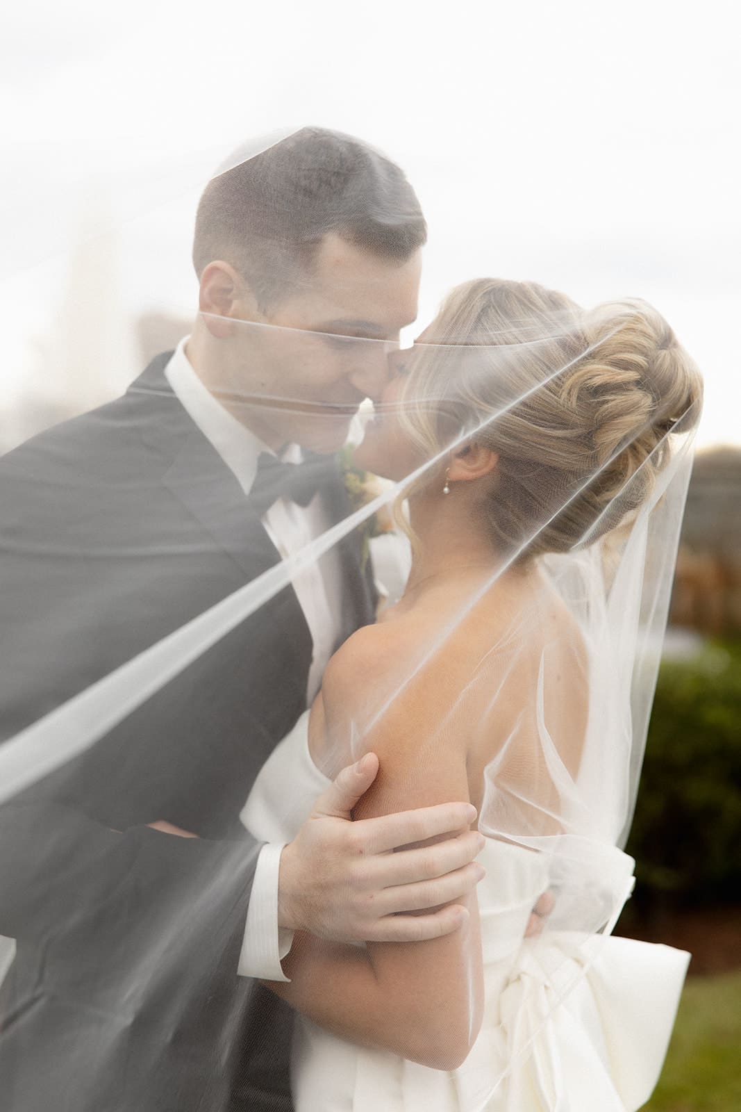 Romantic portrait of bride and groom kissing beneath the veil during an outdoor wedding portrait session.
