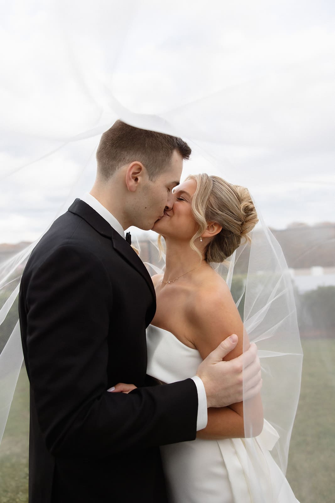 Close portrait of the bride and groom sharing a kiss under the veil on their wedding day.
