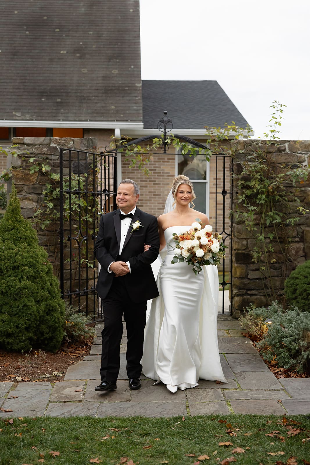 Bride walking down the aisle with her father through a garden gate during an outdoor ceremony at one of the romantic Wedding Venues in Rhode Island.
