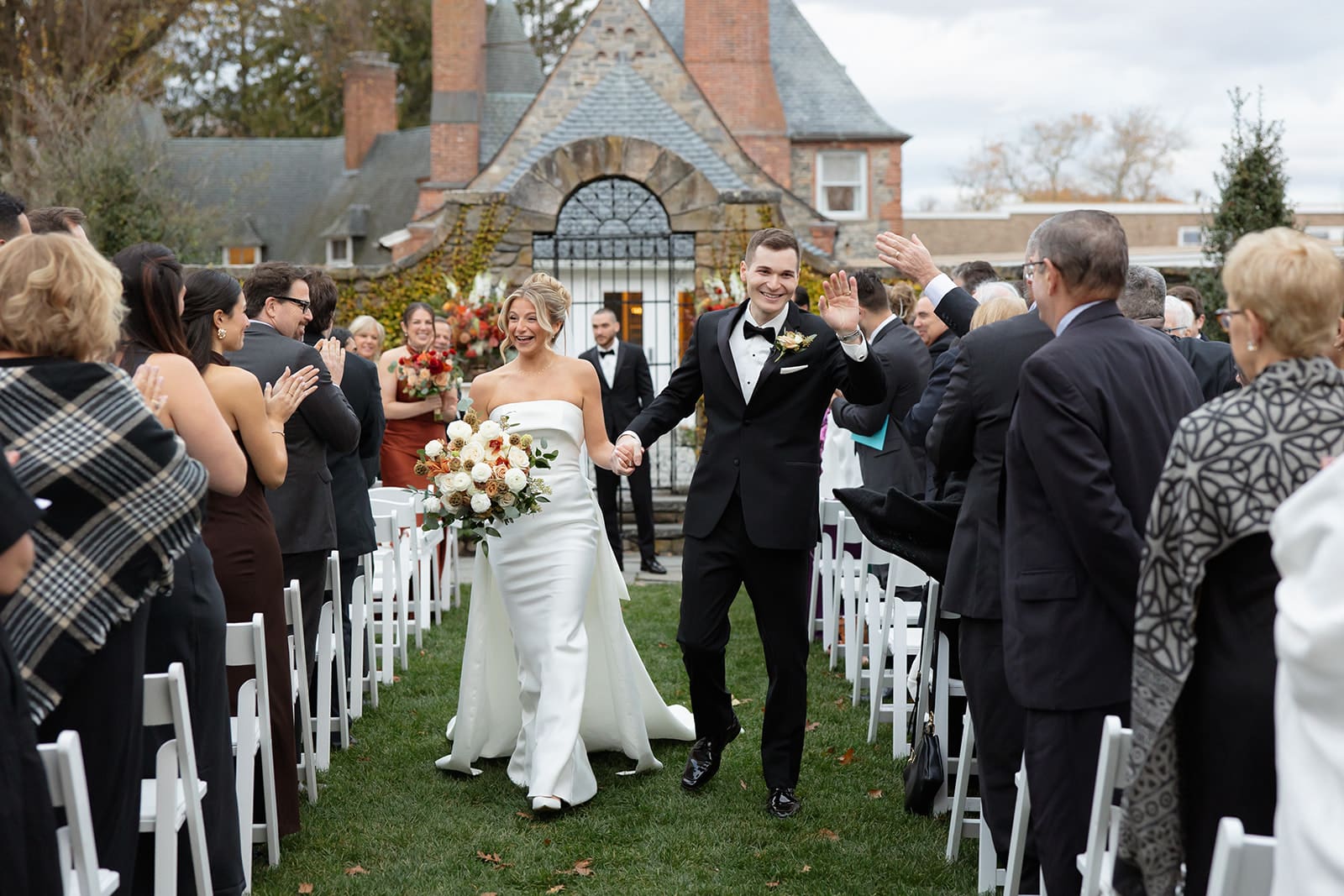 Bride and groom celebrating their recessional while guests applaud during an outdoor wedding ceremony.
