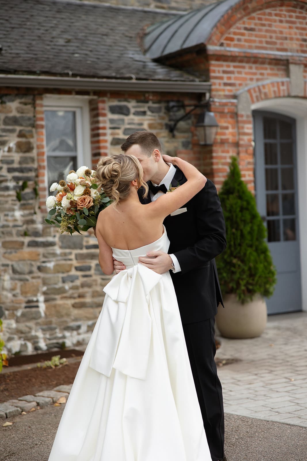 Bride and groom embracing and kissing outside a stone estate wedding venue with fall florals.
