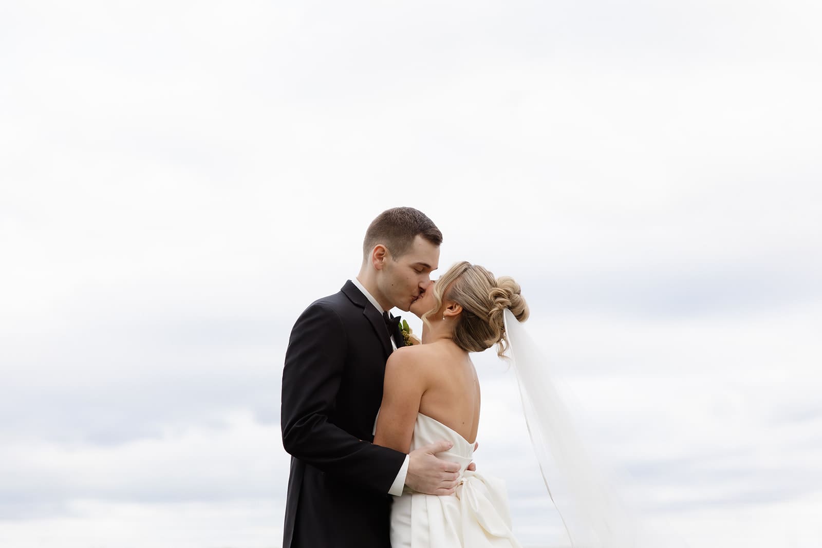 Bride and groom embracing during an outdoor portrait with soft sky tones at one of the scenic Wedding Venues in Rhode Island.
