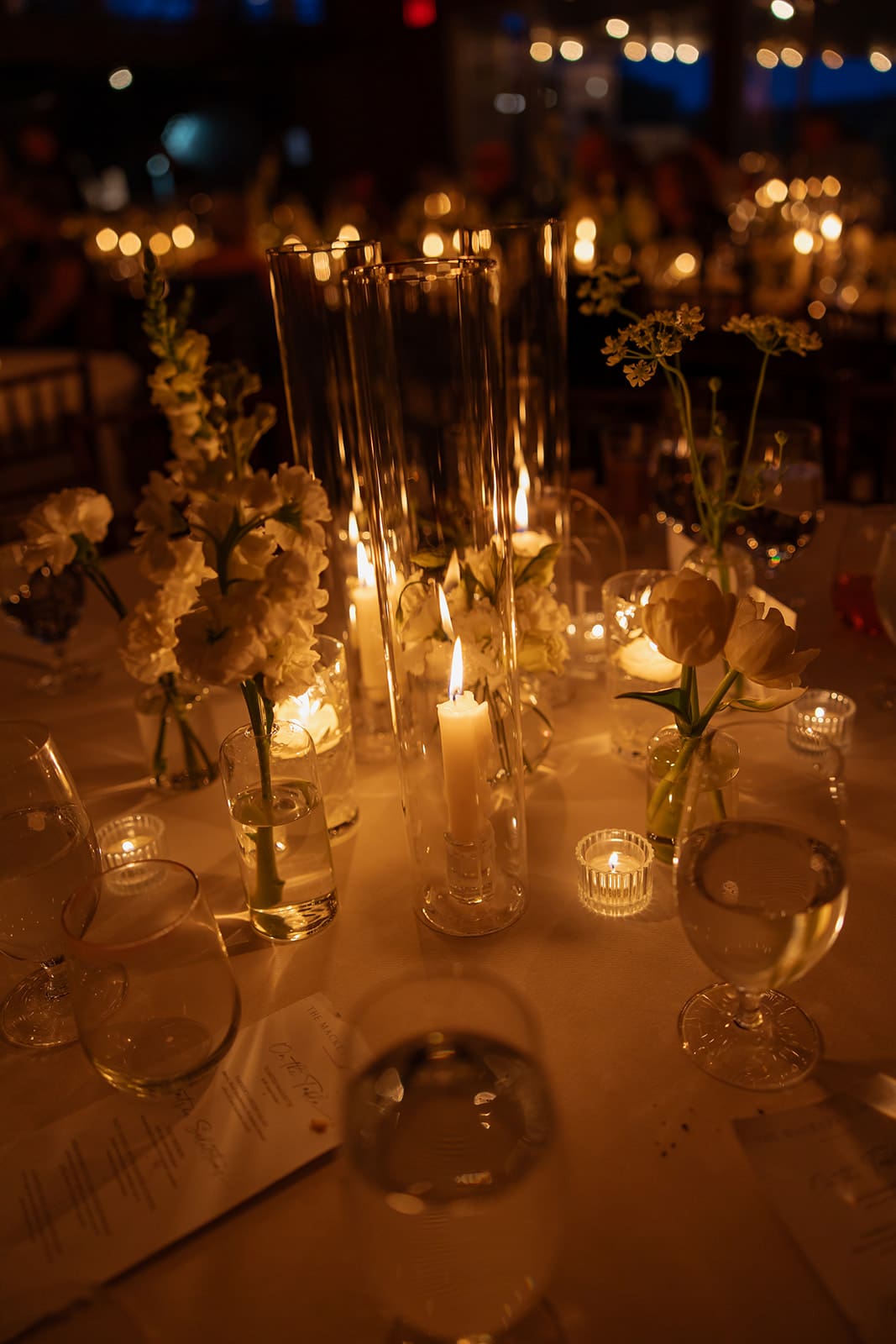 Candlelit wedding reception table with glass cylinder centerpieces and soft evening lighting
