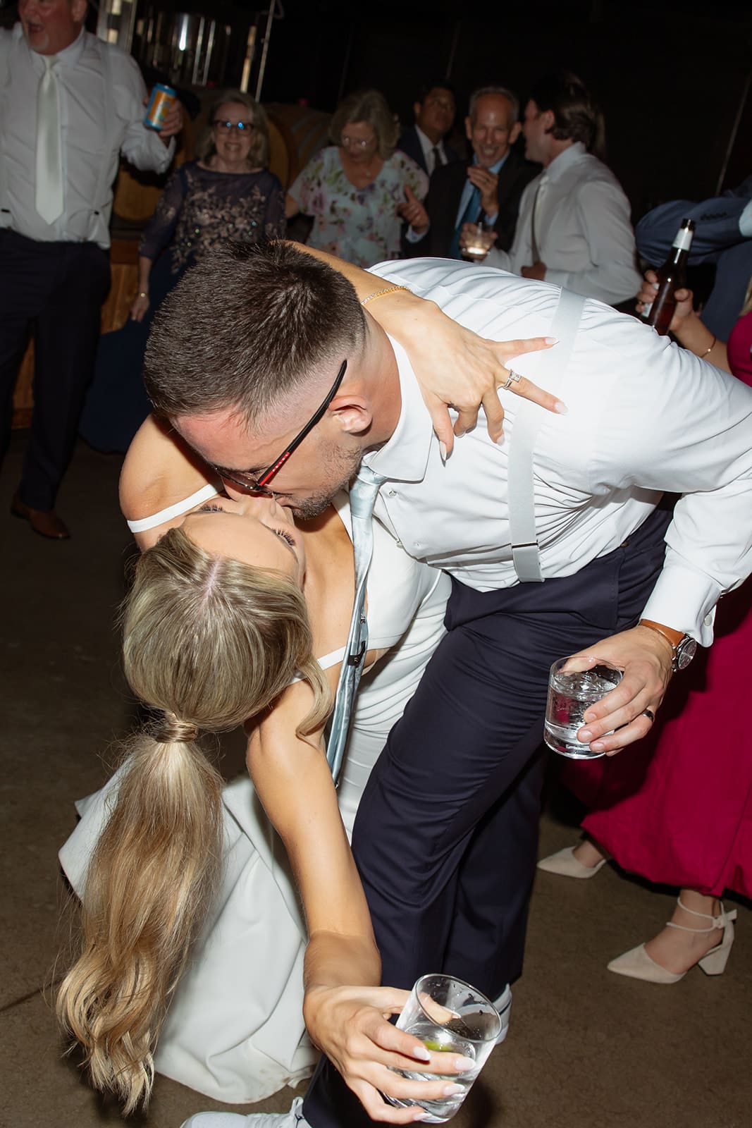 Bride and groom dipping for a kiss while dancing together on the reception dance floor surrounded by guests.