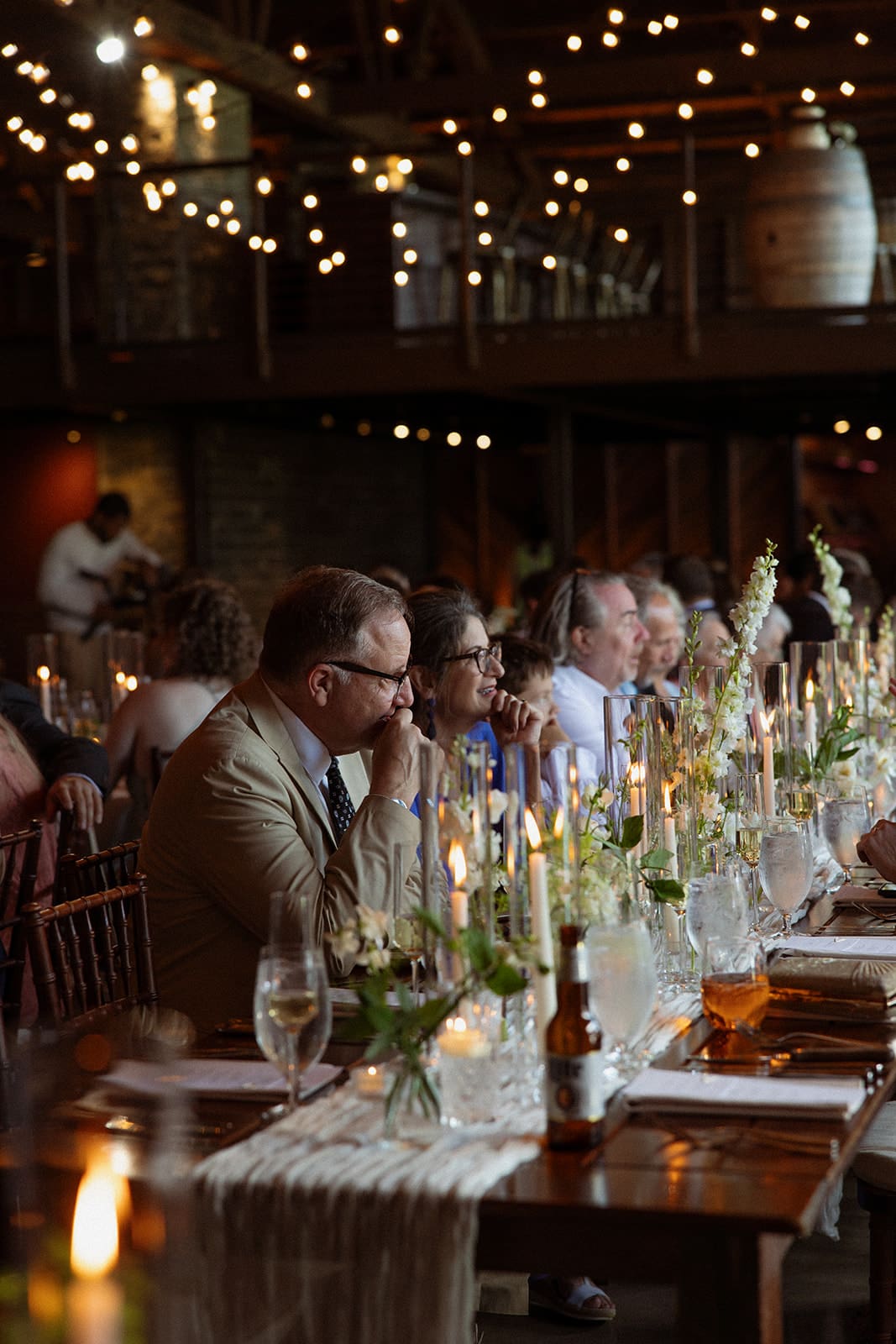 Guests seated at candlelit reception tables inside a warm, rustic Connecticut wedding venue
