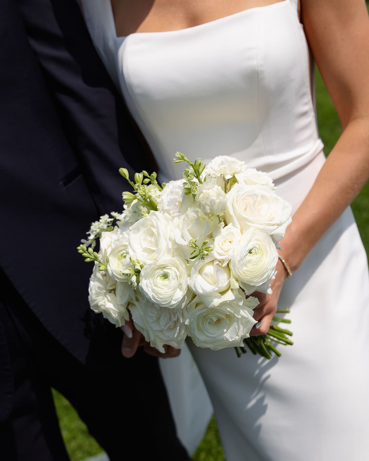Close-up of bride holding white rose and ranunculus bouquet during wedding portraits
