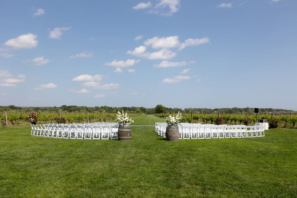 Outdoor ceremony setup with white chairs and floral barrels overlooking vineyard rows at a Connecticut wedding venue.
