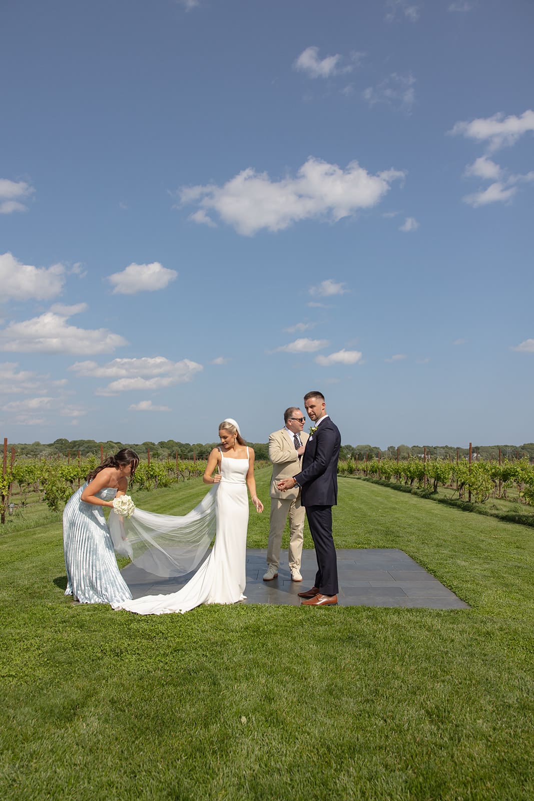 Bride adjusting veil with bridesmaid before ceremony begins in vineyard setting
