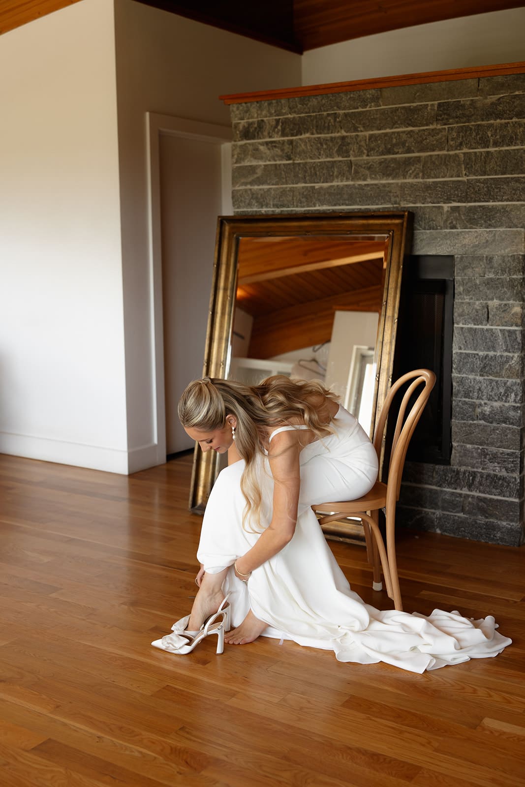 Bride putting on wedding heels in bridal suite with hardwood floors and fireplace
