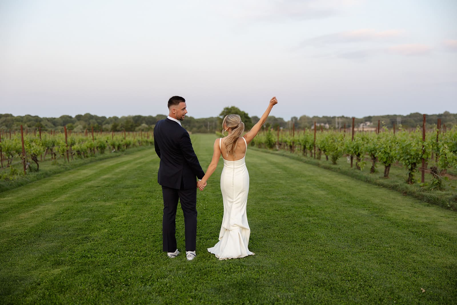 Newly married couple walking hand in hand down a vineyard path at sunset at a Connecticut wedding venue.
