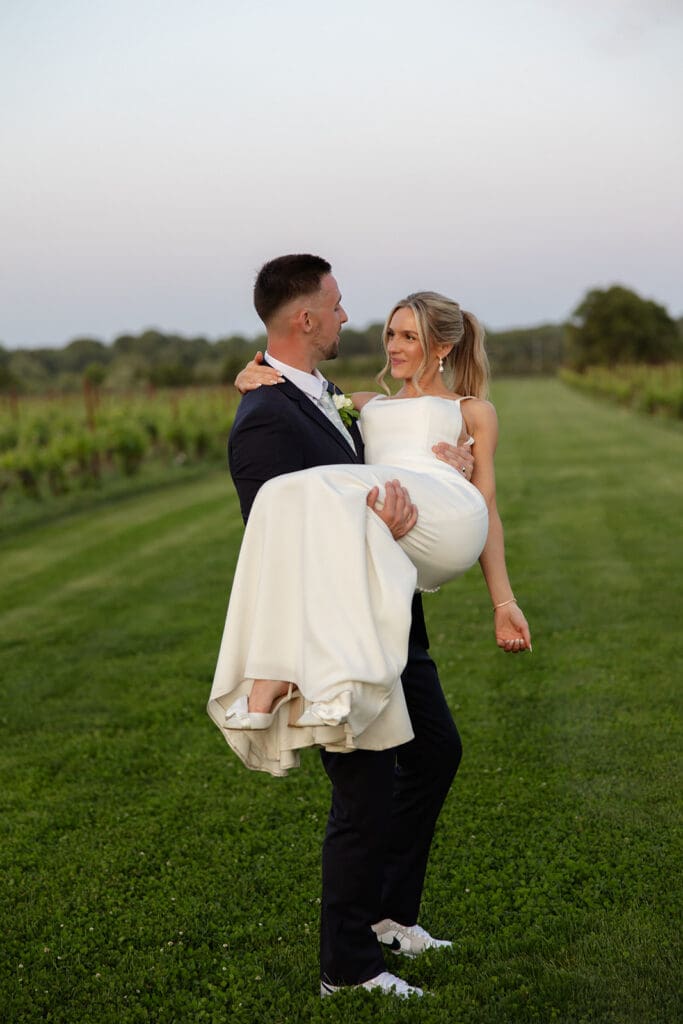 Groom carrying bride across vineyard lawn during golden hour portraits at a Connecticut wedding venue
