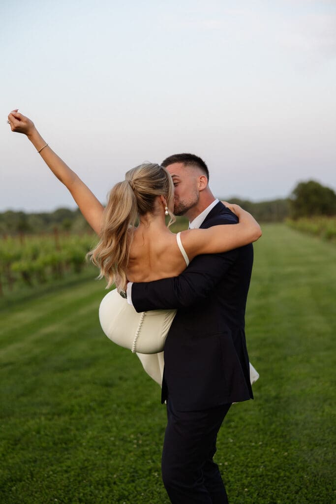 Groom lifting bride during playful sunset portrait in the vineyard

