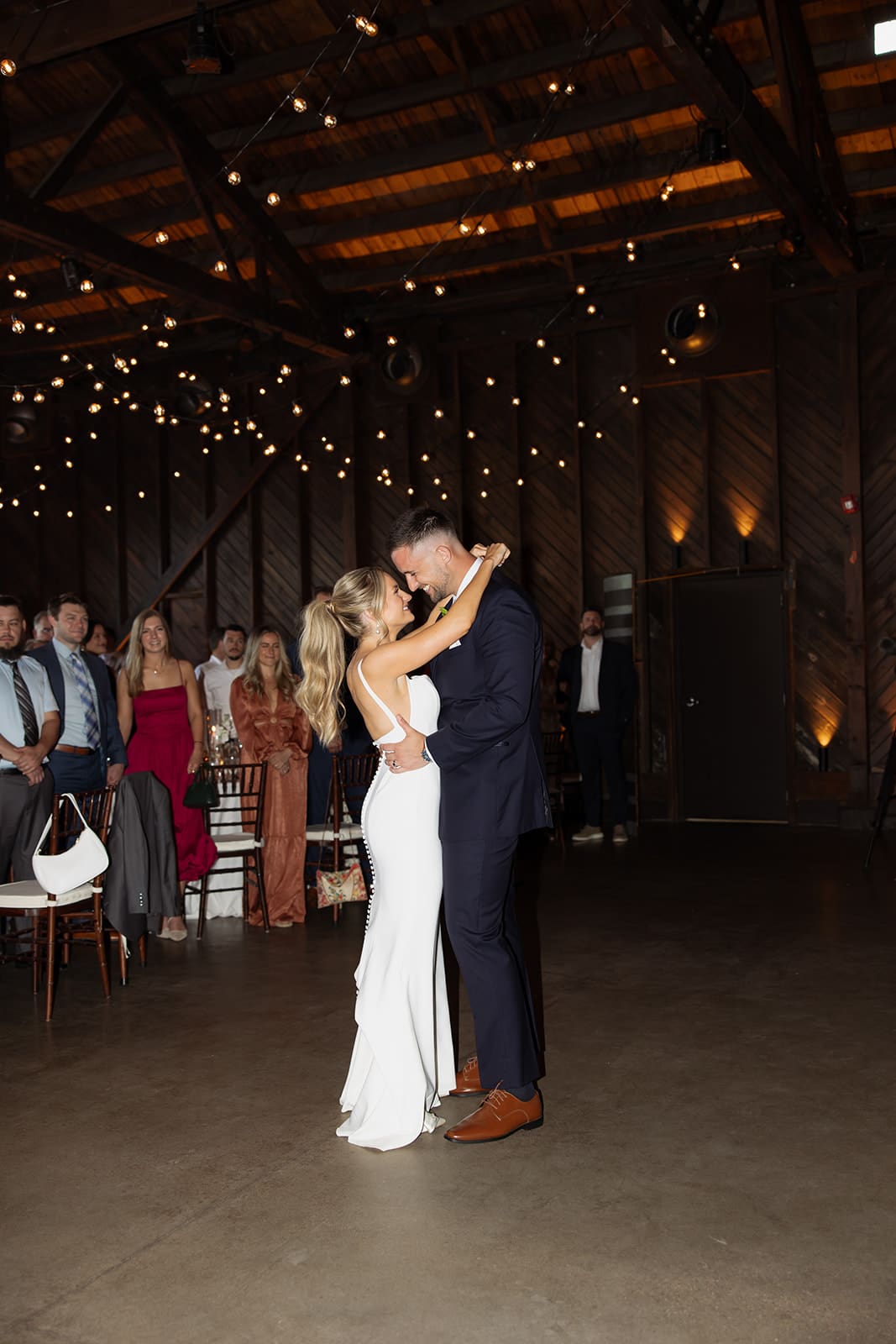 Couple sharing their first dance under twinkle lights inside a wooden Connecticut wedding venue
