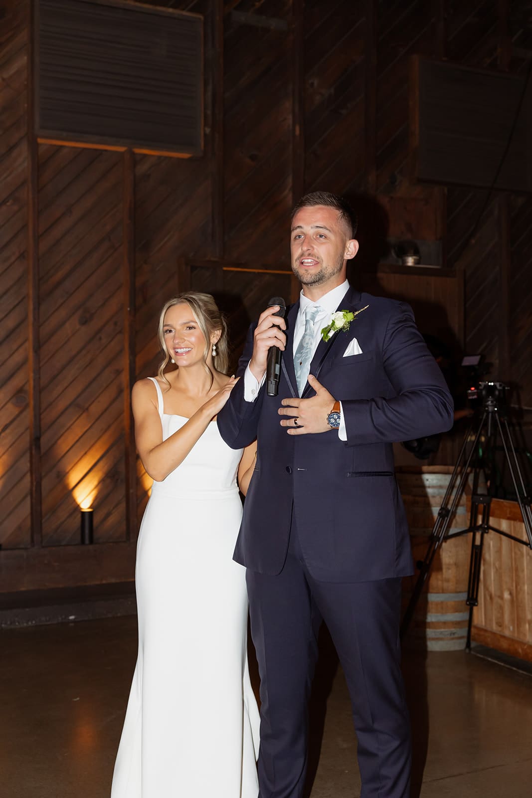 Groom giving reception speech while bride smiles beside him inside a rustic Connecticut wedding venue
